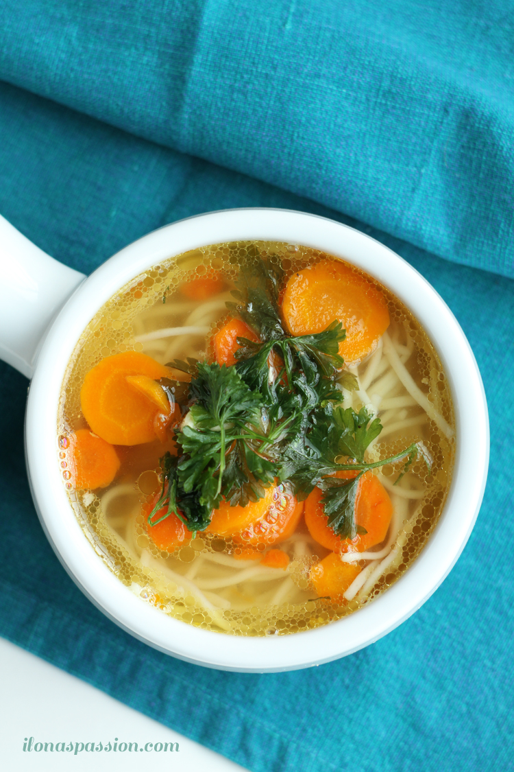 A bowl of chicken soup with carrots, noodles, and topped with fresh parsley