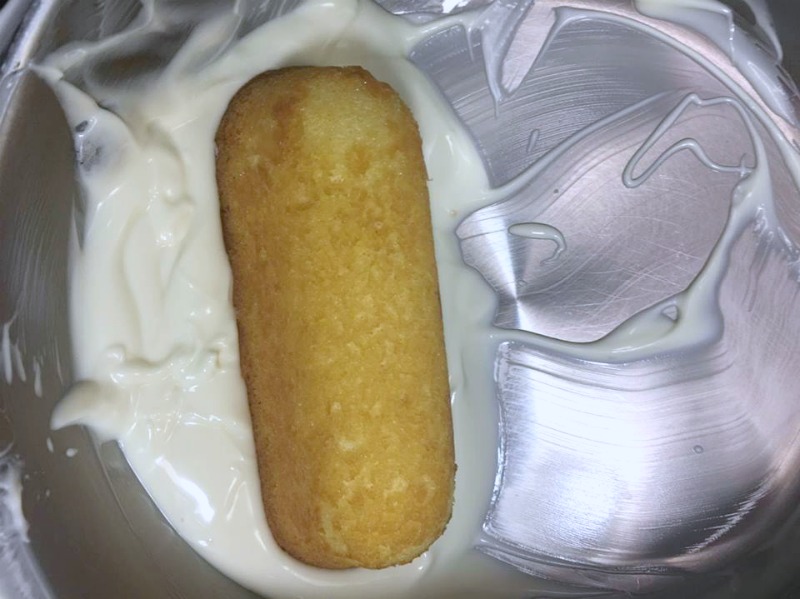 Melted white chocolate in a bowl with a twinkie dipped inside