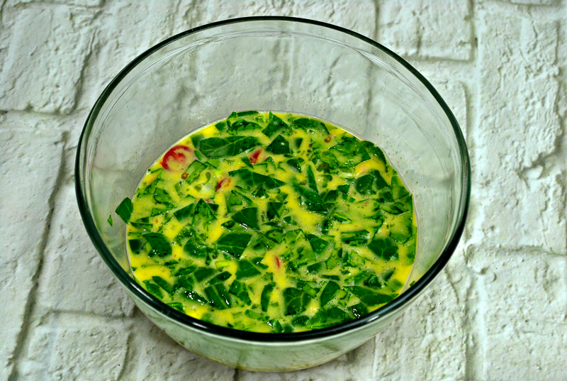 raw eggs in a bowl with tomatoes and spinach
