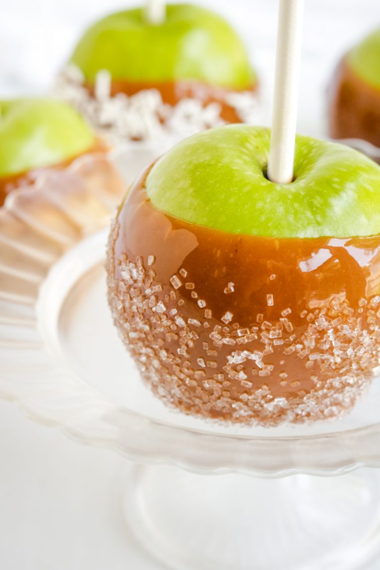 caramel apple with sugar crystals on a plate. Other apples with different toppings in the background