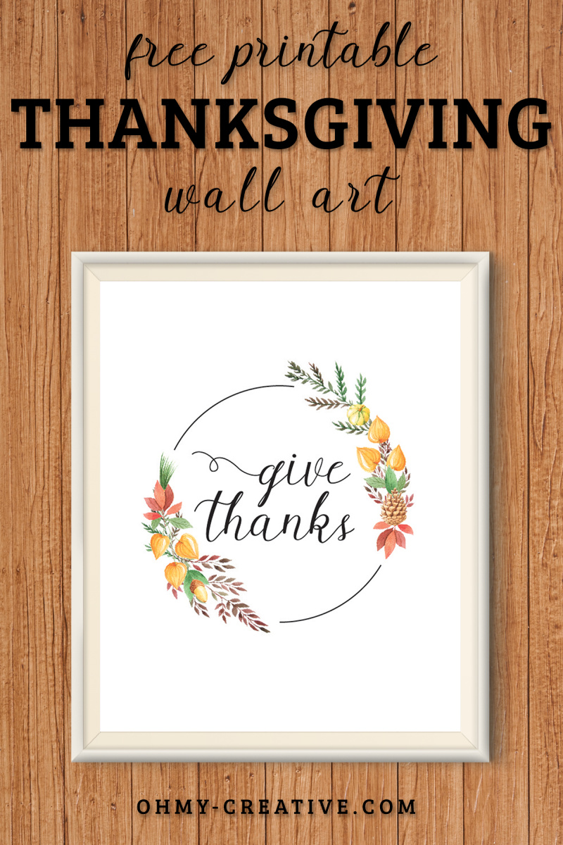 A framed "Give Thanks" printable decoration for Thanksgiving. Displayed on a woodbackground