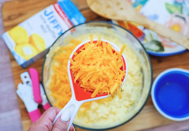 Close up of adding cheddar cheese ingredient to the mixing bowl for the corn casserole with Jiffy.