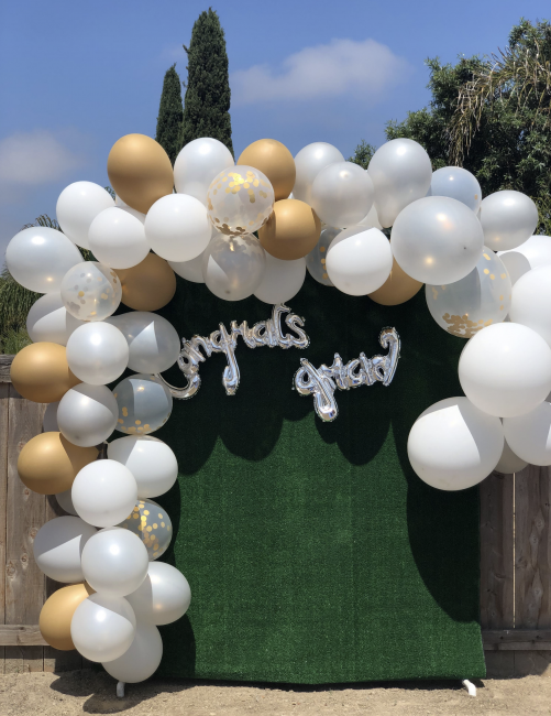 Green photo booth back drop with gold and white balloon garland. Congrats Grad silver balloon is attached to the backdrop.