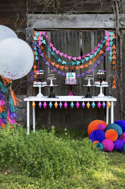 This outdoor graduation party dessert table is magical using bright colors, paper garlands and pretty cake plates to display the desserts. Consider adding large confetti balloons and paper spheres to accent the table.