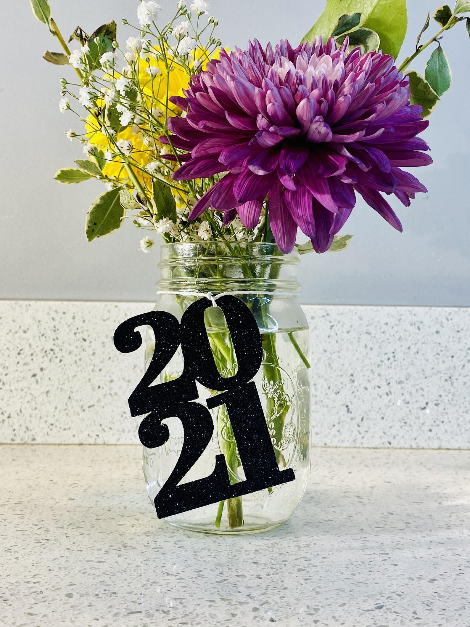 Mason jar filled with colorful flowers and a black 2021 cutout tied onto the mason jar to created a pretty table centerpiece. 