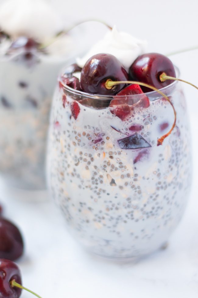 Cherry chia pudding with whole cherries on top with stems on a while table.