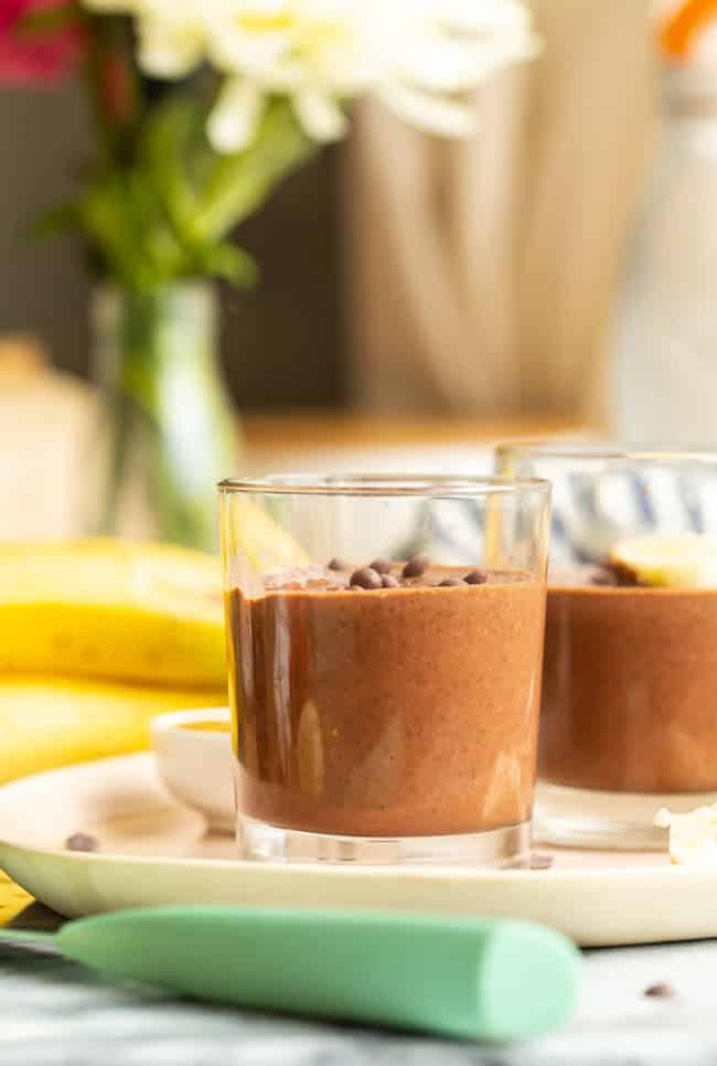 A couple of chocolate peanut butter chia puddings on a table. A vase of flowers sits in the background.