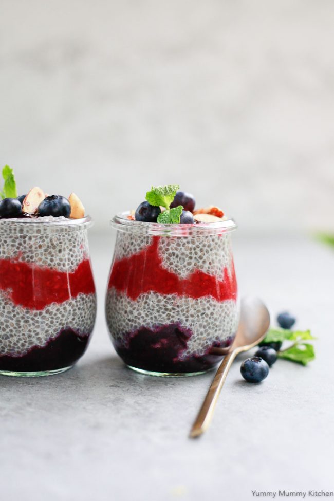 These two berry chia puddings are decorated with fresh berries and a gold spoon.
