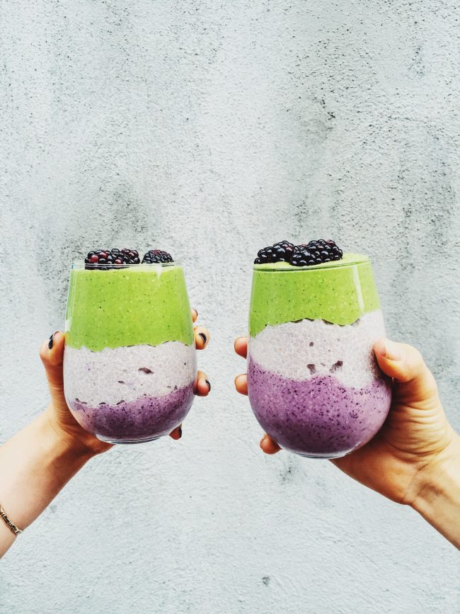 Two hands each holding a blackberry kiwi chia pudding.