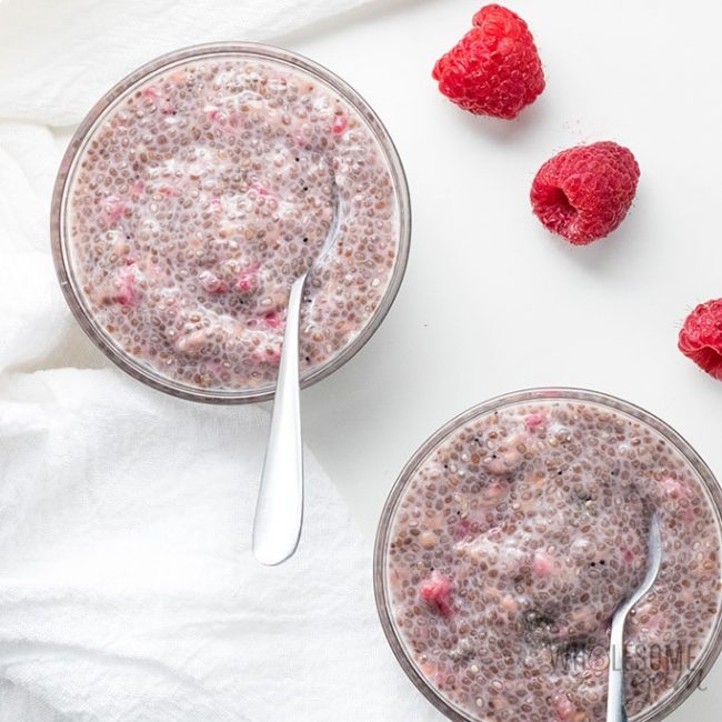 This raspberry low carb keto chia pudding is surrounded by fresh berries. Looking down on the raspberry chia pudding with spoons dipped in for a bite.