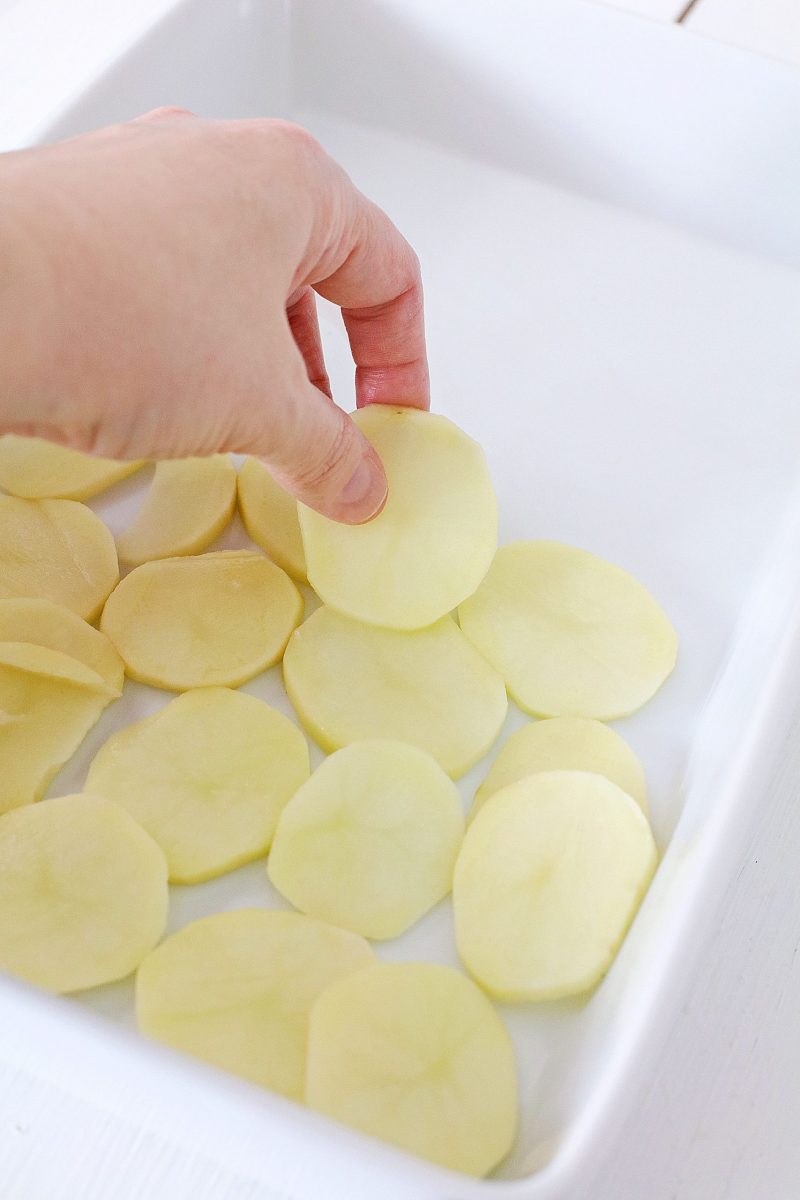 Layer the sliced potatoes evenly in the casserole dish.