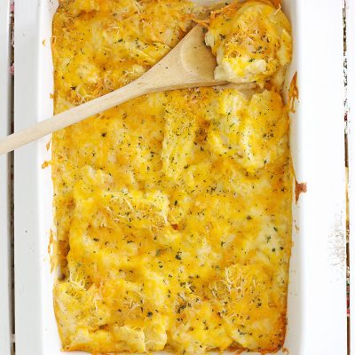 Baked cheesy scalloped potatoes casserole dish fresh out of the oven sitting on a white background.