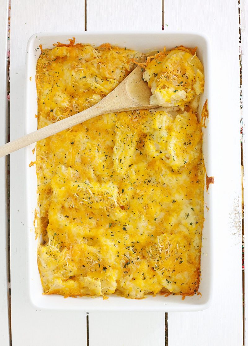 Baked cheesy scalloped potatoes casserole dish fresh out of the oven sitting on a white background. 