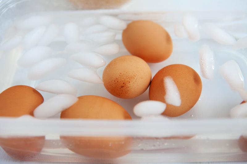 Brown eggs are cooling in a clear bowl with added ice cubes.
