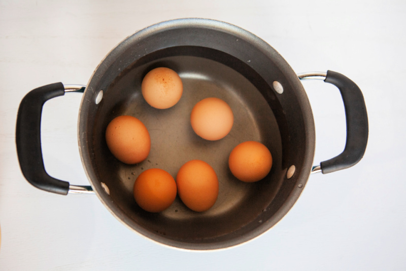 Brown eggs boiled in a black pot of hot water.