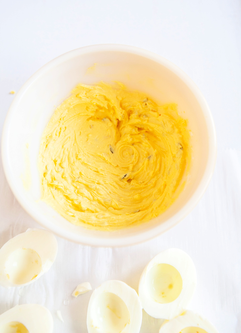Cooked egg yolks blended together with other ingredients in a white bowl. Cooked egg whites are surrounding the bowl.