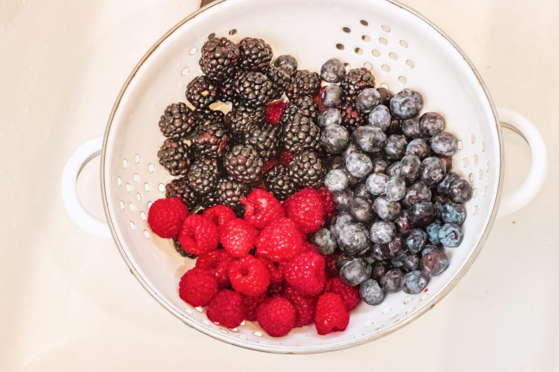 Washed raspberries, blackberries and blueberries in a white strainer.