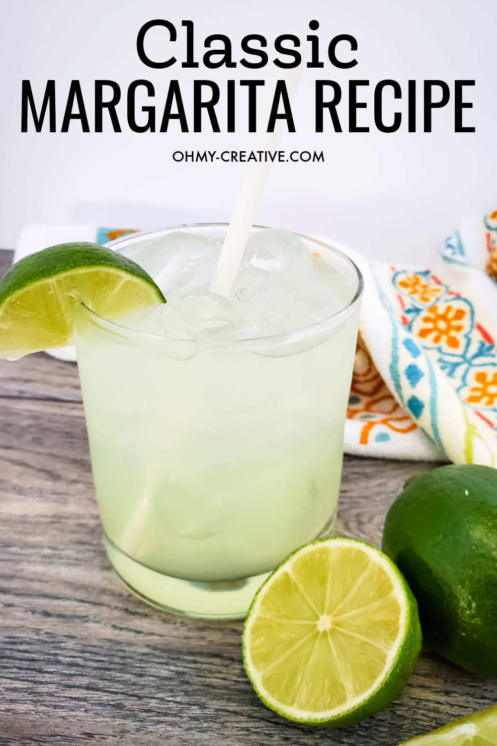 A tasty classic margarita in a tumbler glass with straw garnished with fresh limes. This tasty drink sits on a wood table with a decorative napkin in the background.
