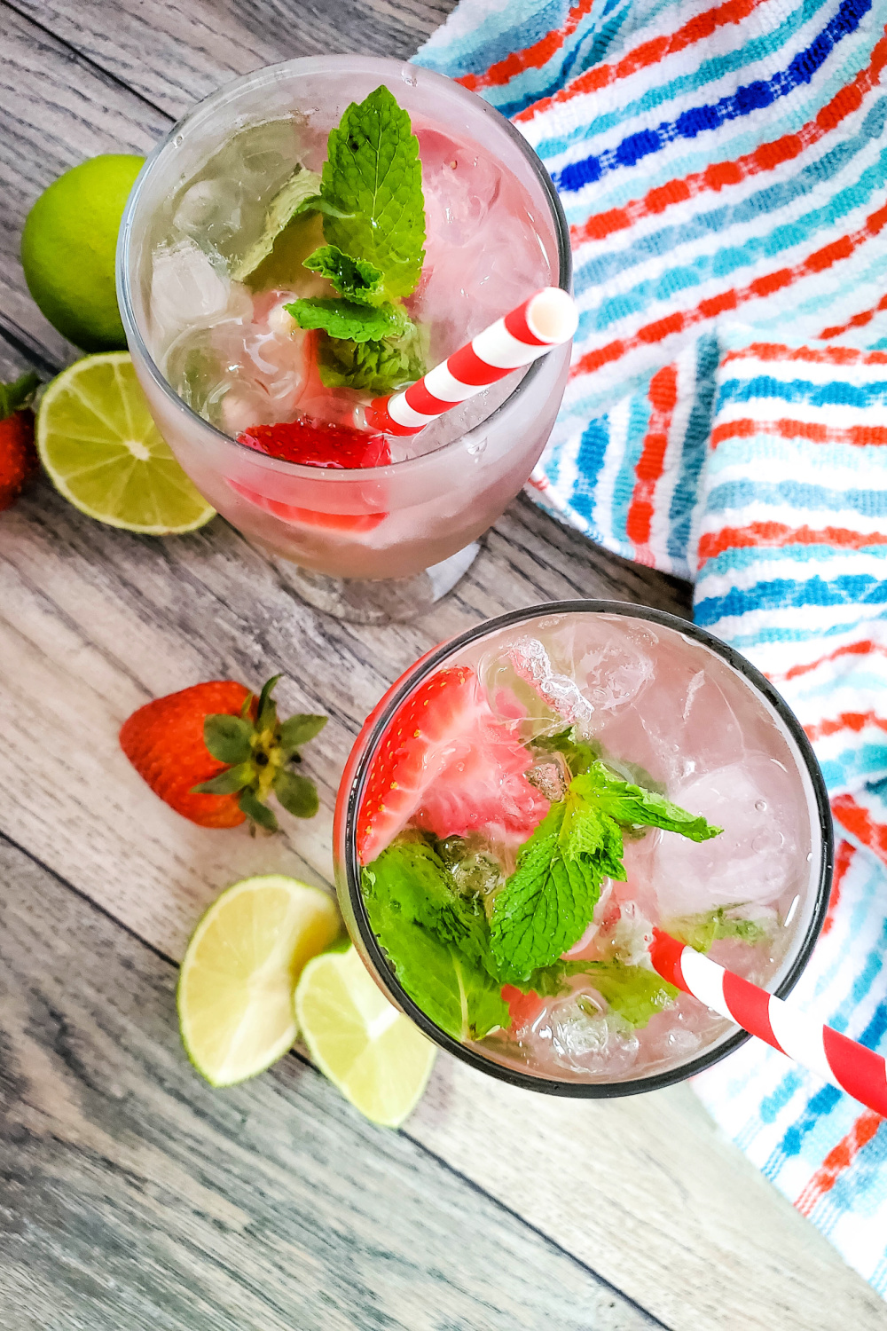 Strawberry mojito cocktail in a clear glass with a red and white paper straw. In the background is a red white and blue striped cloth napkin.