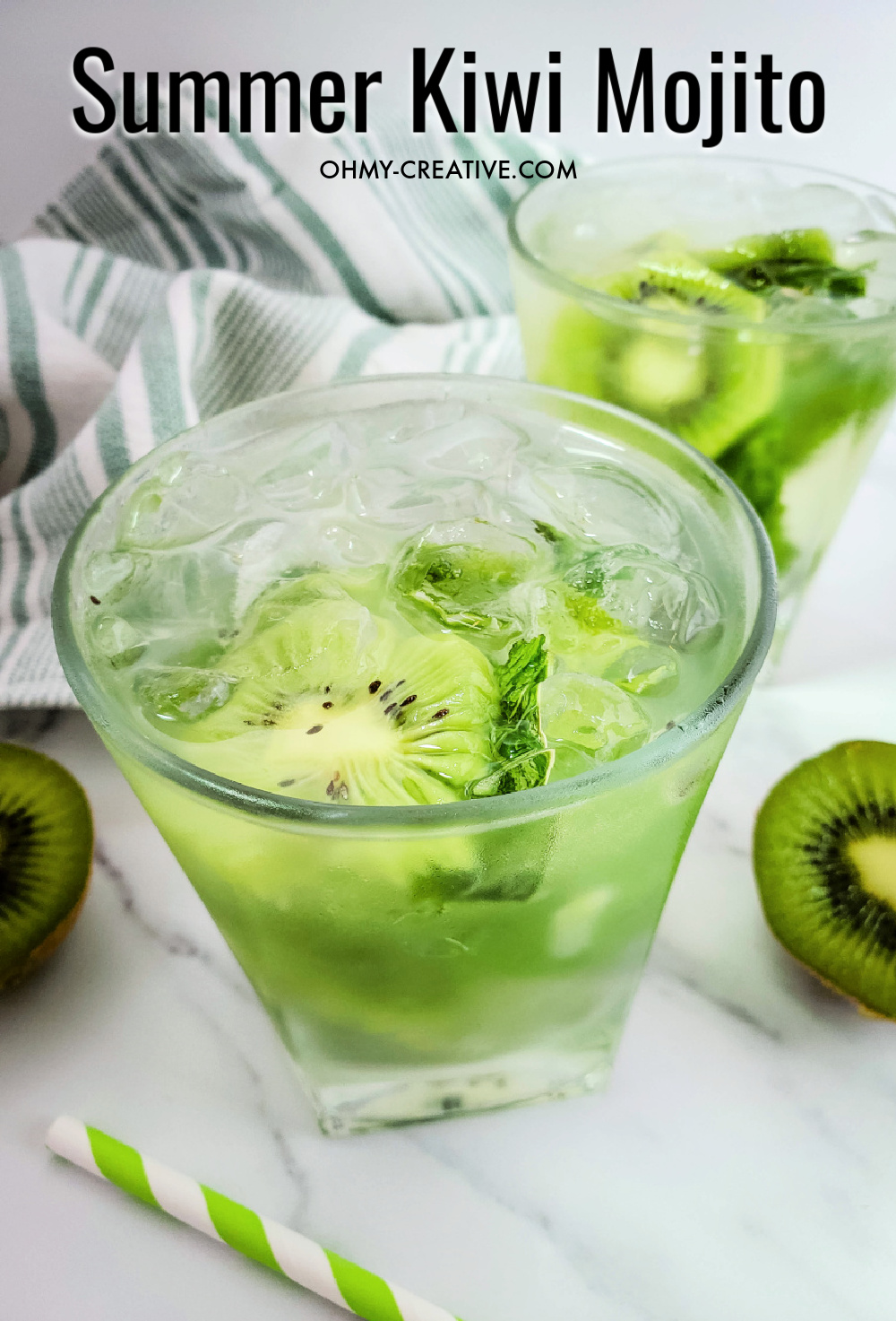 Kiwi mojito drink in a short cocktail glass with sliced kiwi, green and white cloth hand towel and a white marble background.