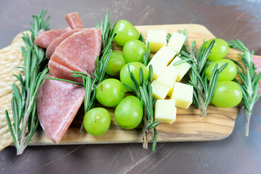 Rosemary, salami, grapes, and mozzarella cheese arranged on a charcuterie board 