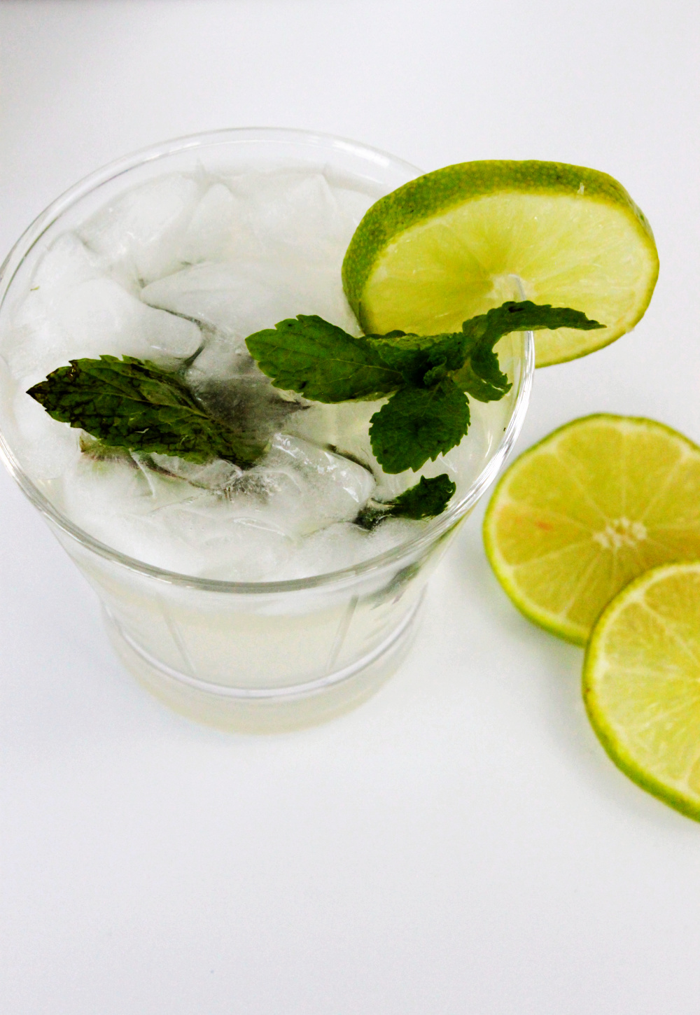 A top view highball glass with a tequila mojito cocktail topped with mint and a slice of a lime. Slice limes are also on the table.
