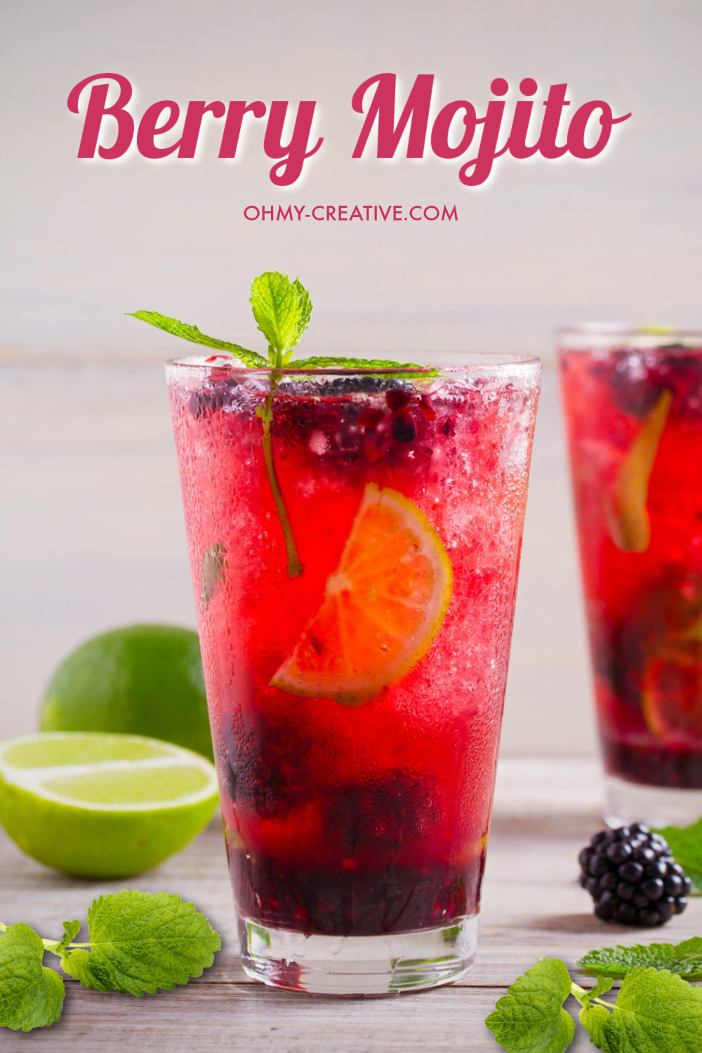 A berry mojito on a gray wood background with sliced limes and mint. This mixed berry mojito is garnished with mint and a slice of lime.