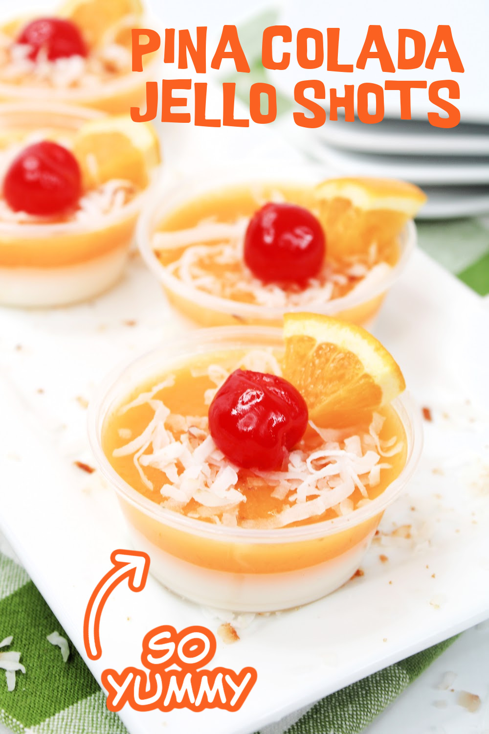 Pina Colada jello shots garnished with coconut and a cherry served on a white plate with a green checked napkin.
