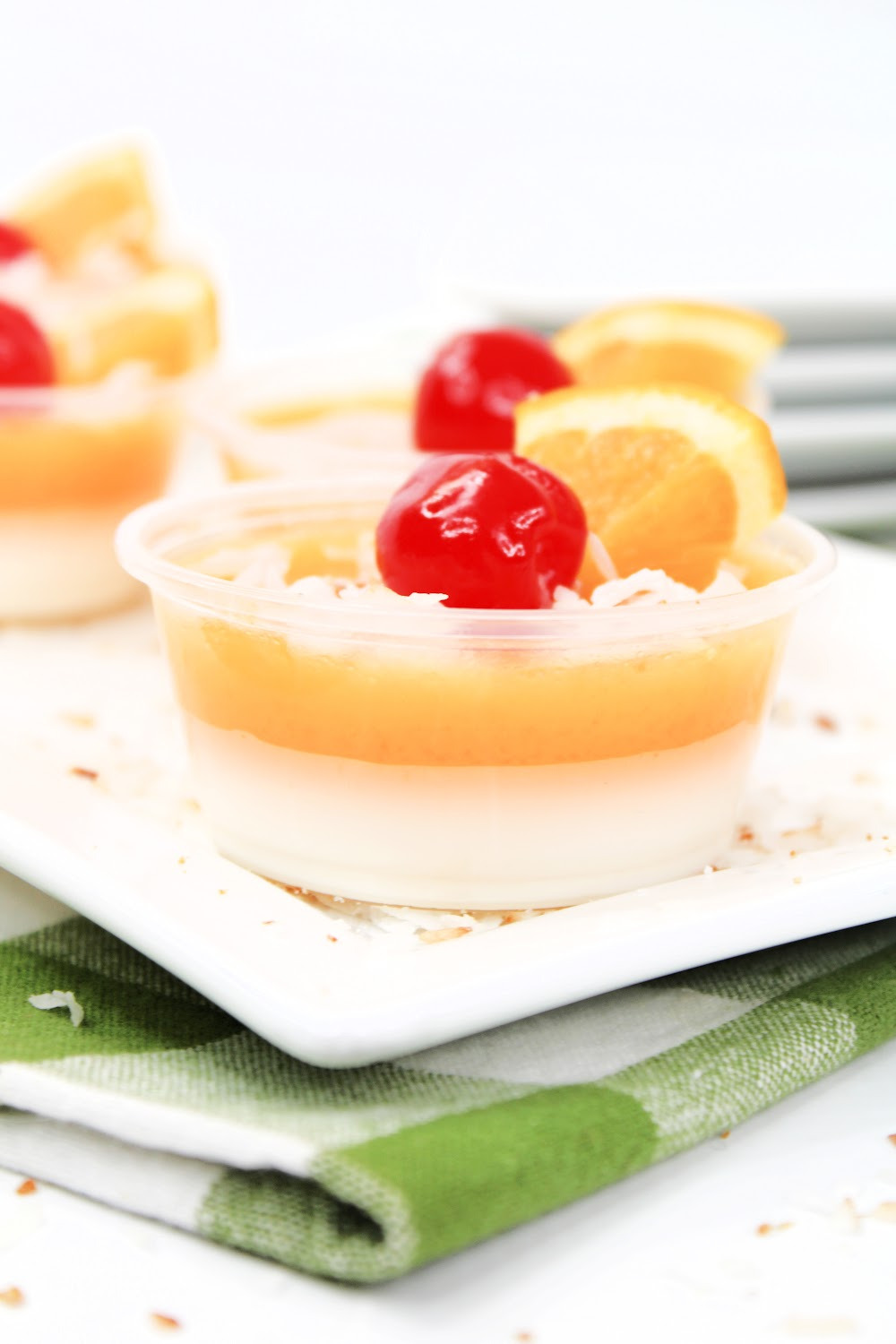A close up of Pina Colada jello shots served on a white plate with a green checked napkin.