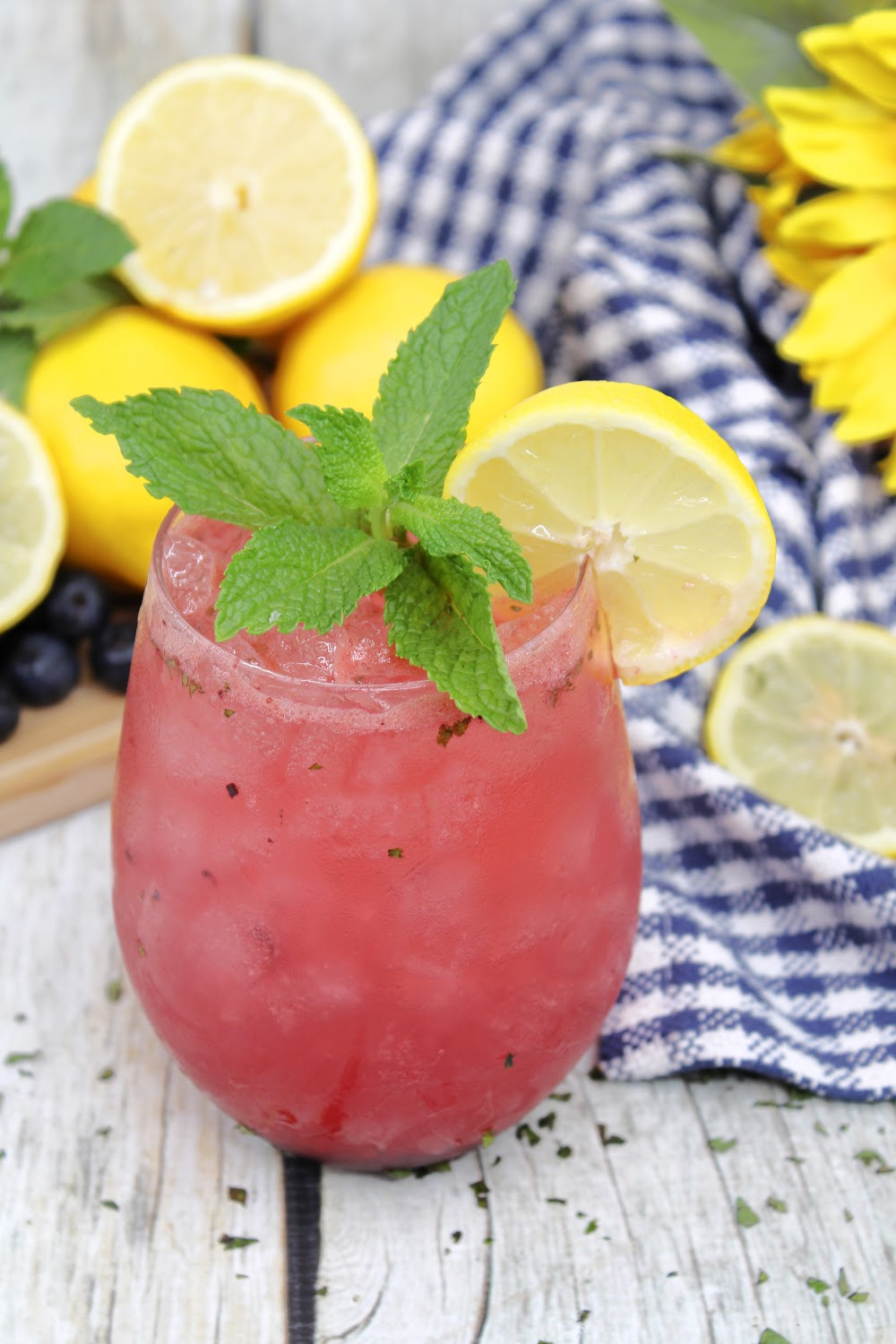 The best flavors of summer are in this blueberry lemonade mojito. Shown here with a blue and white checked napkin with sliced and whole lemons!