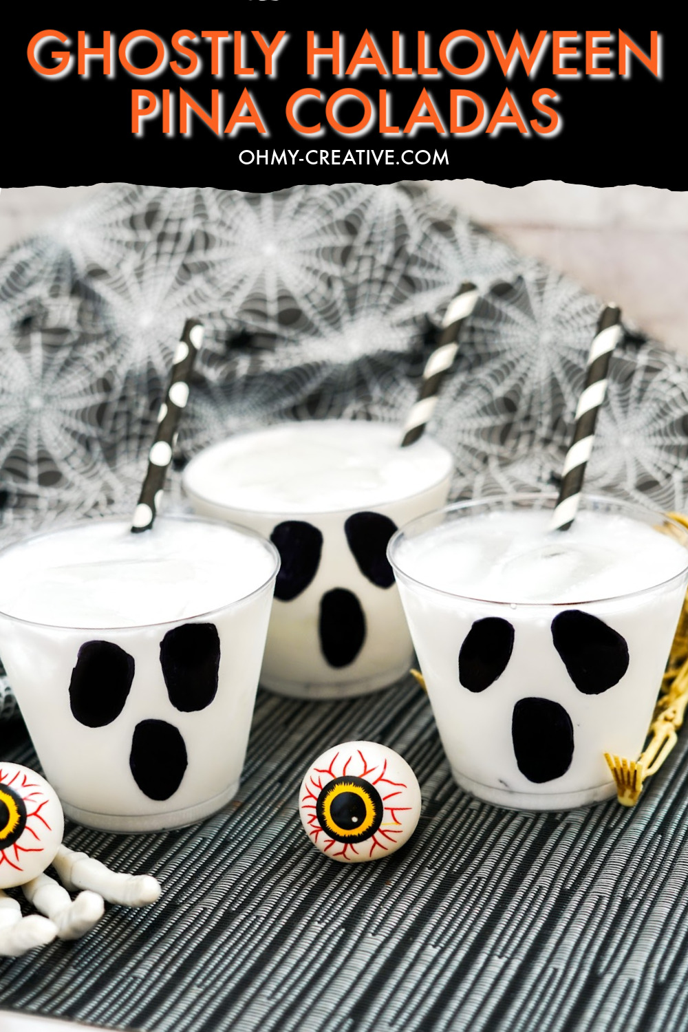 These ghost Halloween pina coladas are sitting on a black and white striped background with a spider web print in the background. Plastic eye balls and skeleton hands make this a spooky Halloween drink!