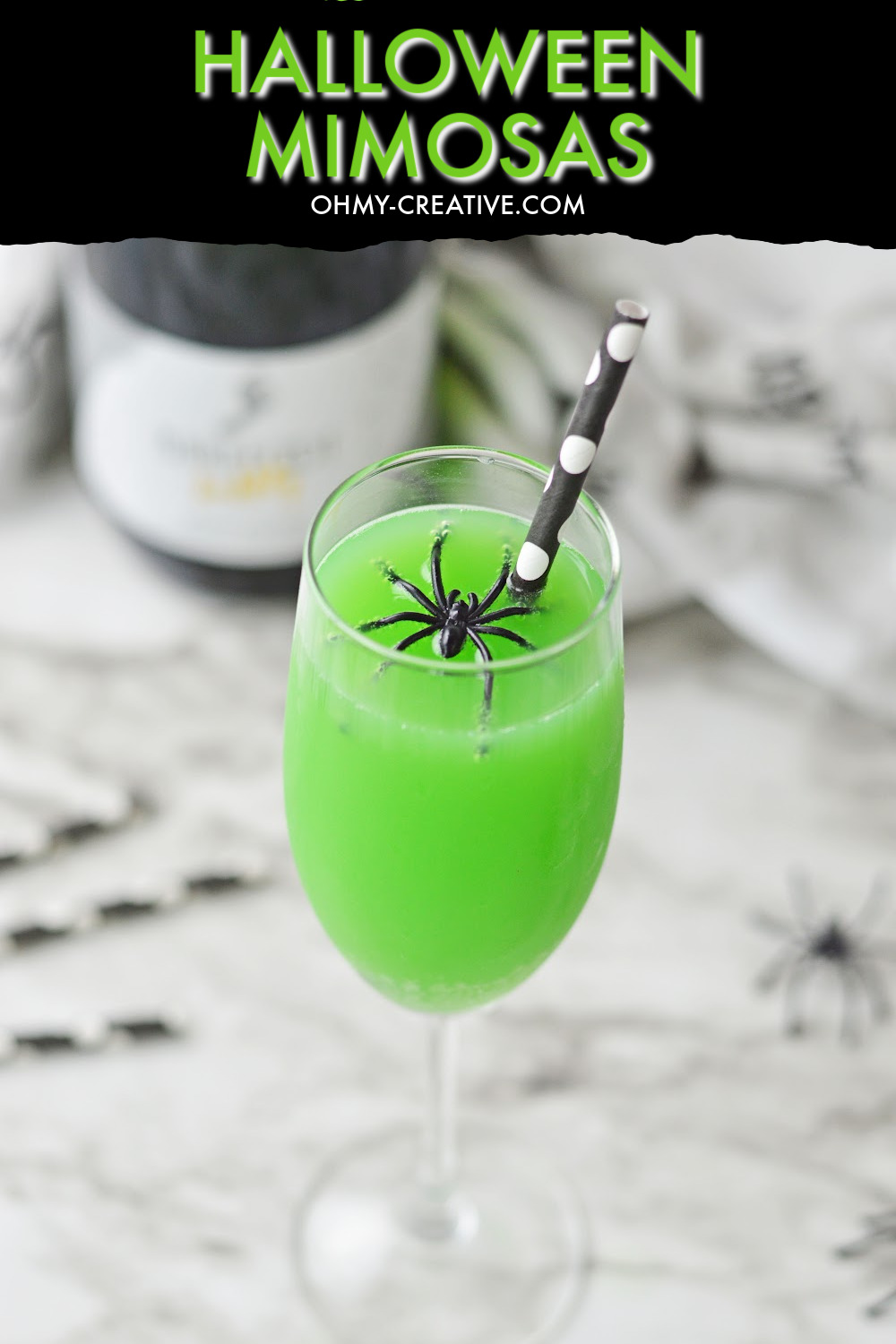 These spooky Halloween Mimosas are displayed on a black and gray marble background with creepy spiders and black and white straws in the background. There is also a champagne bottle in the background.