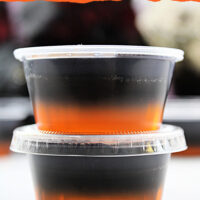 These orange and black layered Halloween jello shots are made with black vodka. The orange jello layer is on the bottom and the black layered made with grape jello and black vodka is on the top. Here they are stacked on top of each other with plenty in the background.