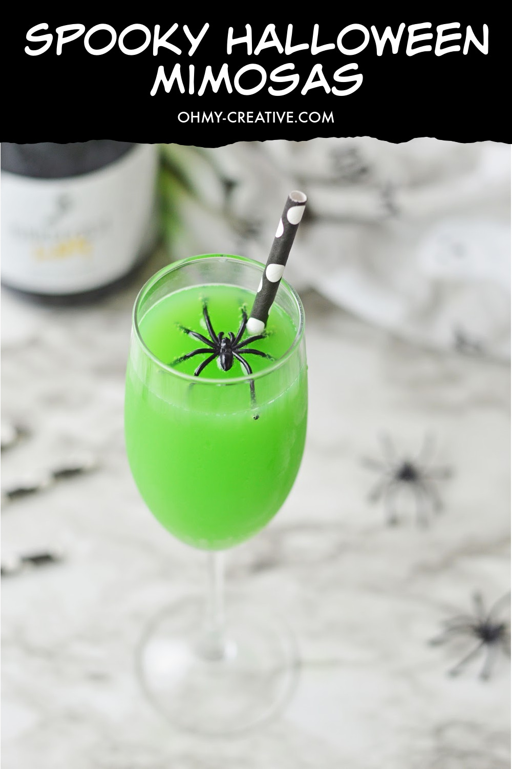 These spooky Halloween Mimosas are displayed on a black and gray marble background with creepy spiders and black and white straws in the background.