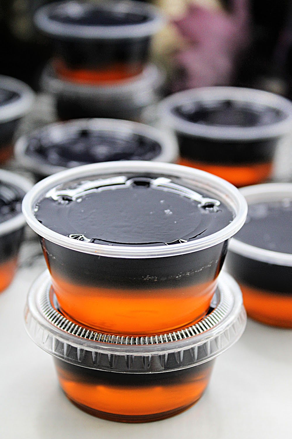 These orange and black layered Halloween jello shots are made with black vodka. The orange jello layer is on the bottom and the black layered made with grape jello and black vodka is on the top. Here they are stacked on top of each other with plenty in the background.