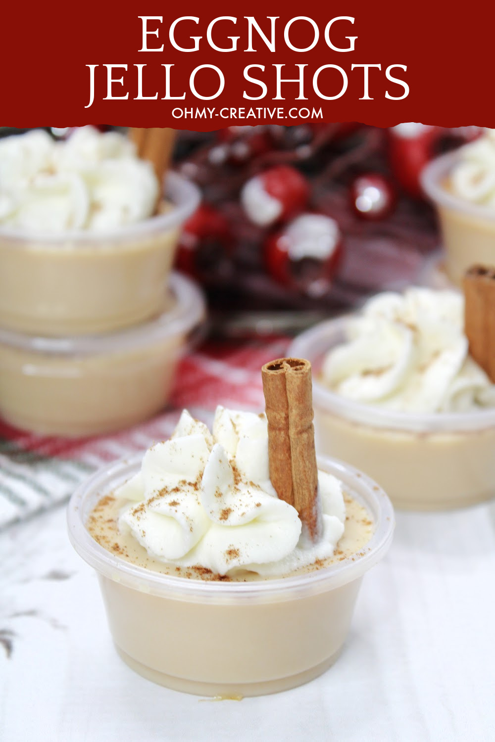 Rich and creamy eggnog jello shots topped with whipped cream a sprinkle of nutmeg and garnished with a cinnamon stick.