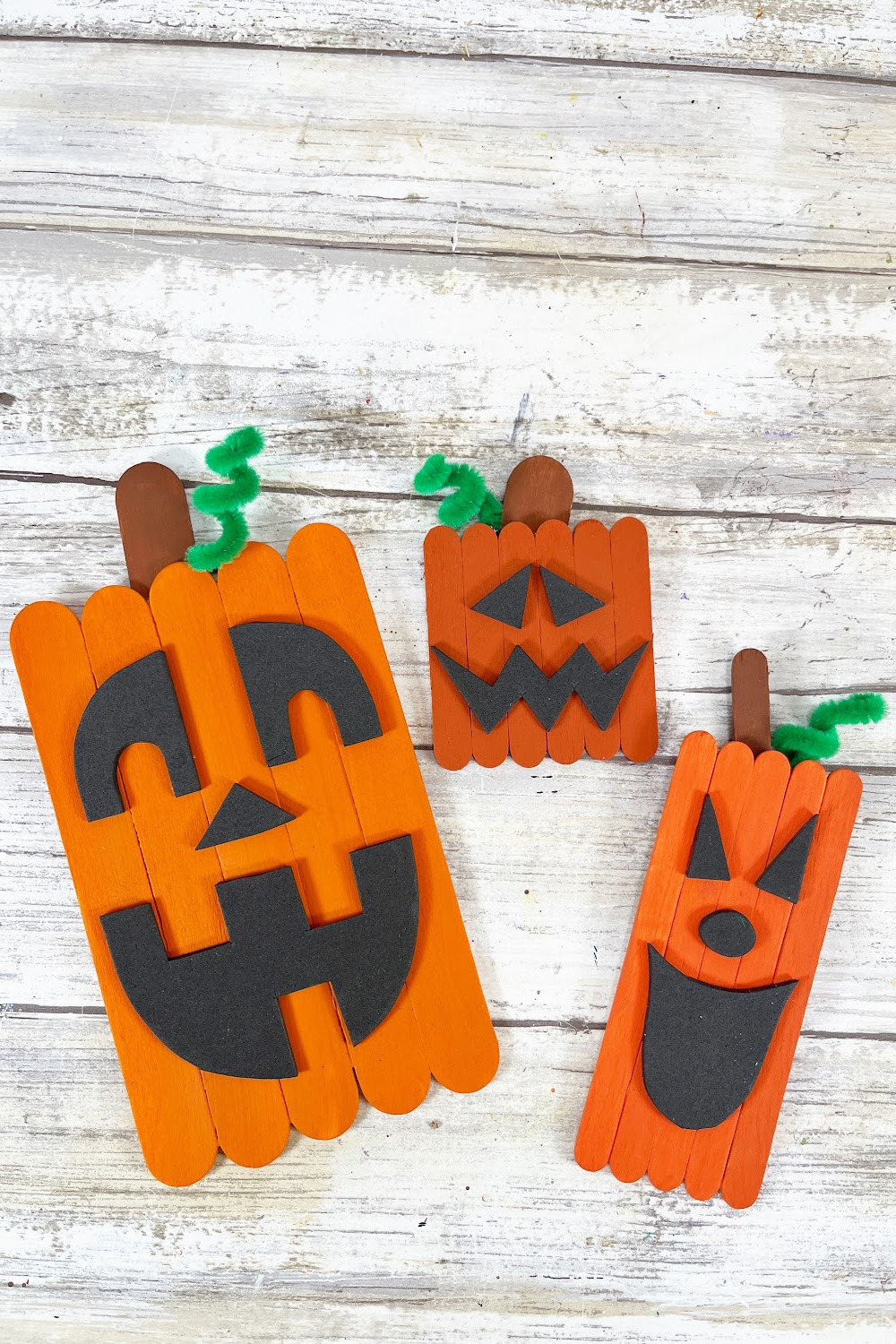 Three popsicle stick pumpkins laying on a wood background.