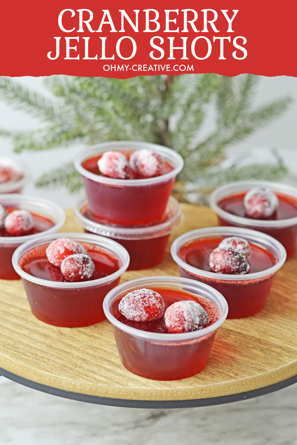 Serve up this tasty cranberry jello shots for the holidays! These Christmas jello shots are sitting on a wood tray with Christmas greenery in the background.