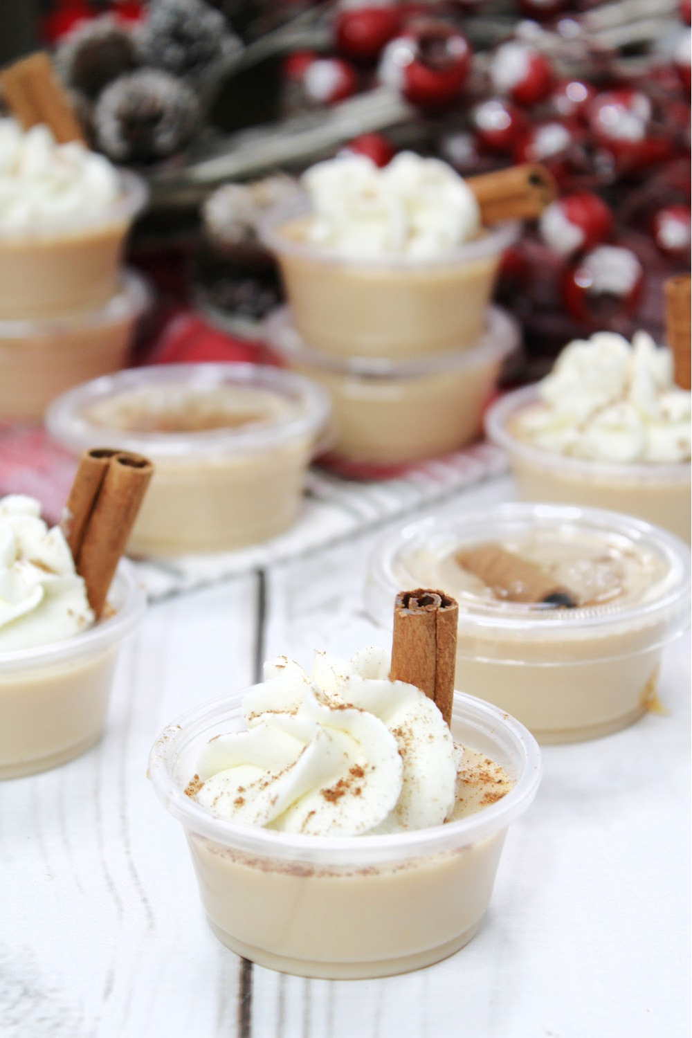 Several Rich and creamy eggnog jello shots topped with whipped cream a sprinkle of nutmeg and garnished with a cinnamon stick.