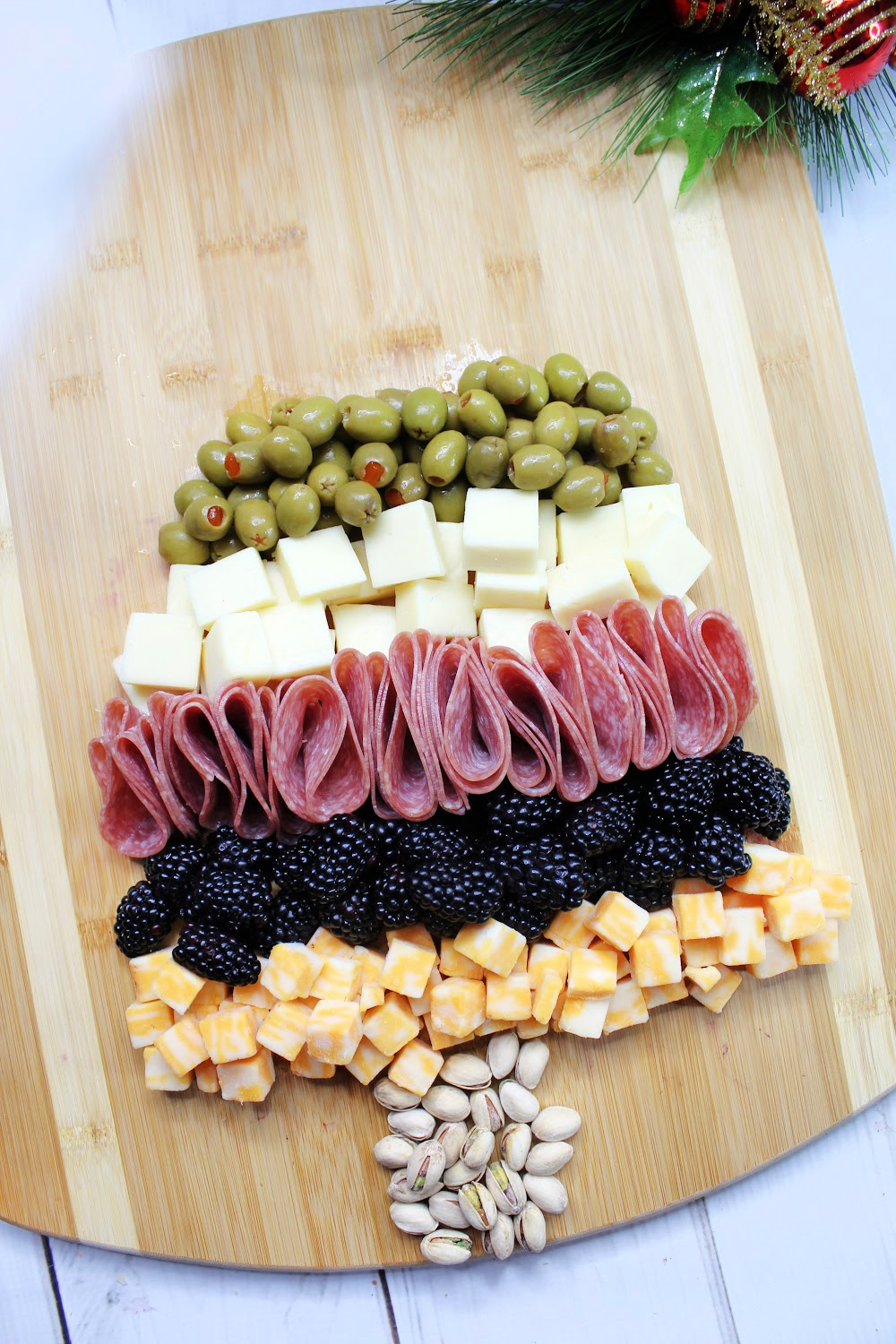 An empty charcuterie board using nuts as the trunk of a Christmas tree. Cheese, meat and berries are the first layers on the shape of the tree.