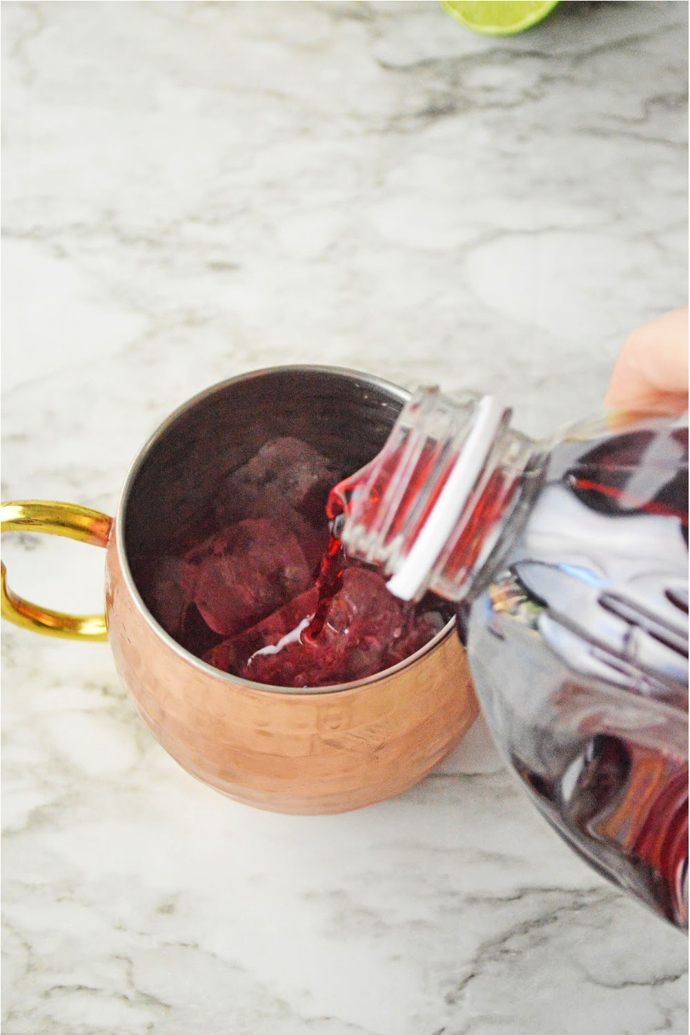 Pouring ingredients into a copper mug to make a cranberry Moscow mule.