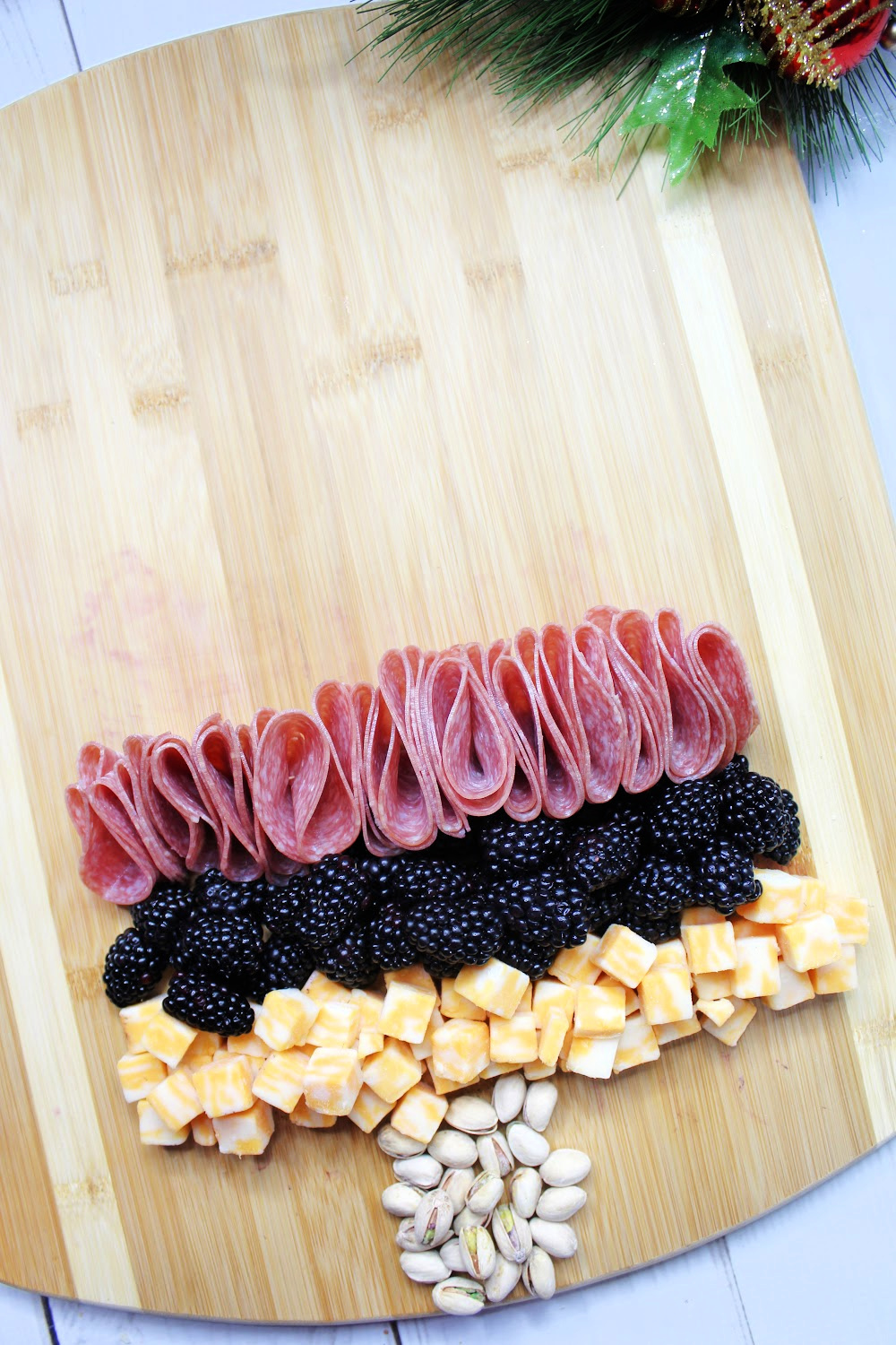 An empty charcuterie board using nuts as the trunk of a Christmas tree. Cheese, meet and berries are the first layers on the shape of the tree.