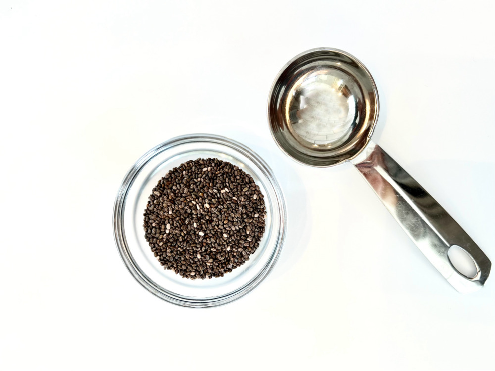 Chia seeds in a glass dish alongside a measuring spoon.
