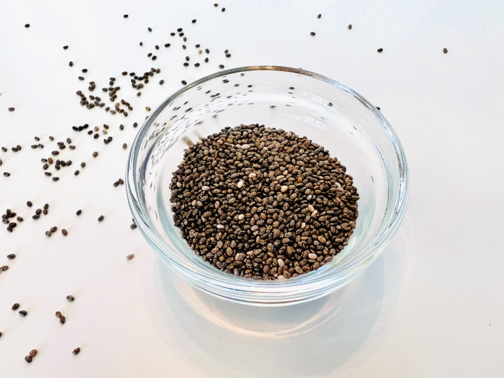 Organic chia seeds in a dish with a few sprinkled on the table.