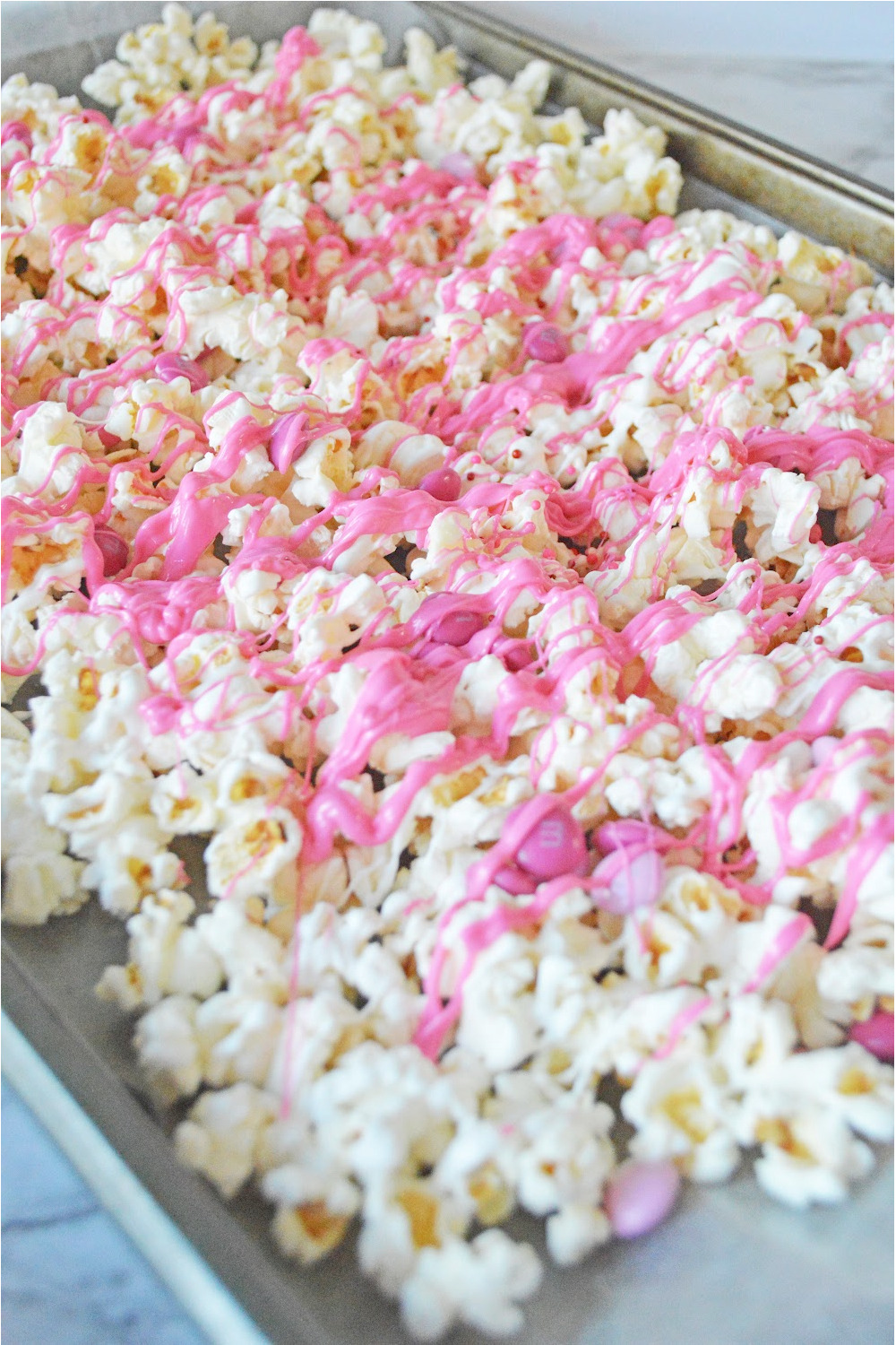 Valentines Popcorn with white and pink candy melts drizzled on top with pink M&Ms.