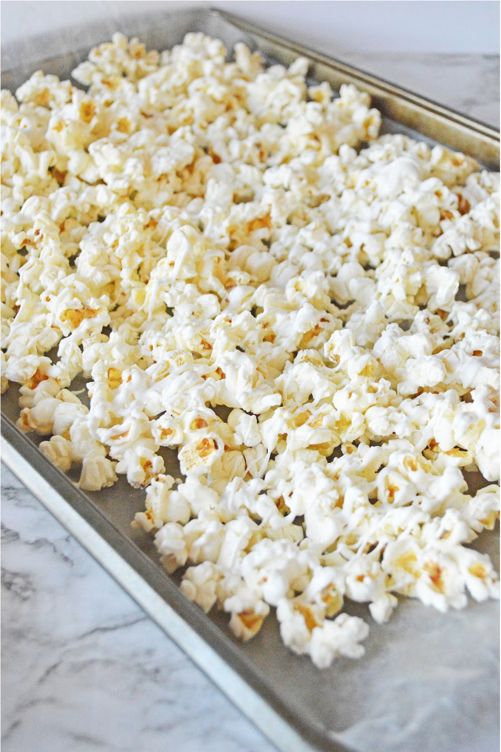 popcorn spread on a baking sheet with white candy melts drizzled on top.