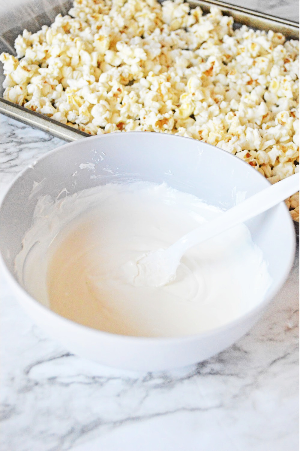 bowl of melted white candy melts ready to drizzle on popcorn with a spoon.