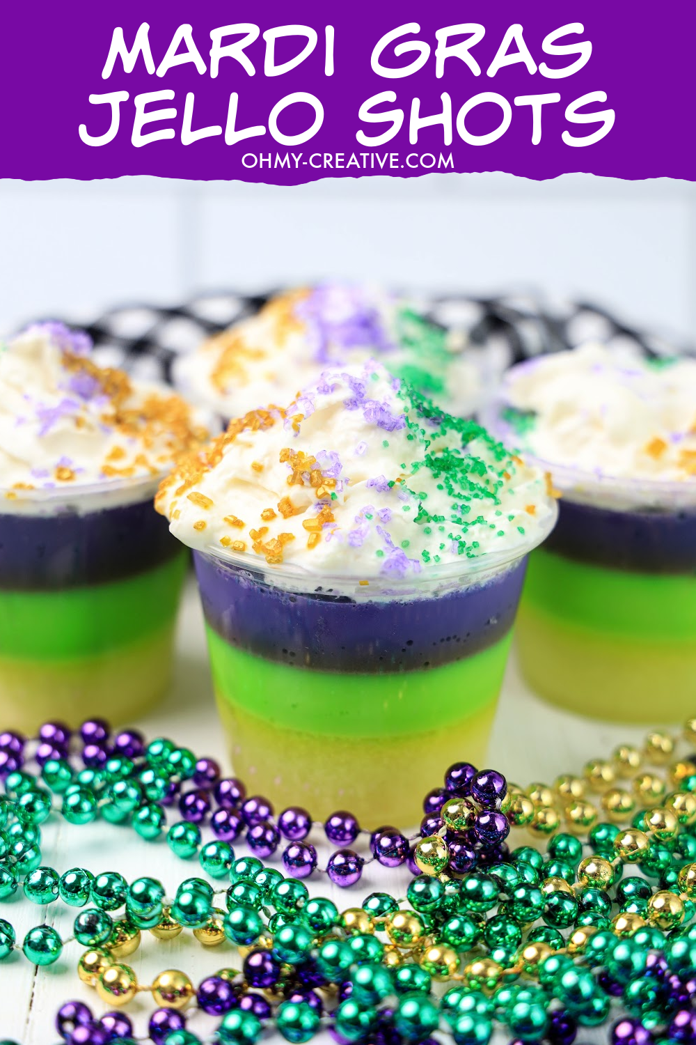 Layered purple, green and yellow Mardi Gras jello shots topped with whipped cream and purple, green and yellow sprinkles.