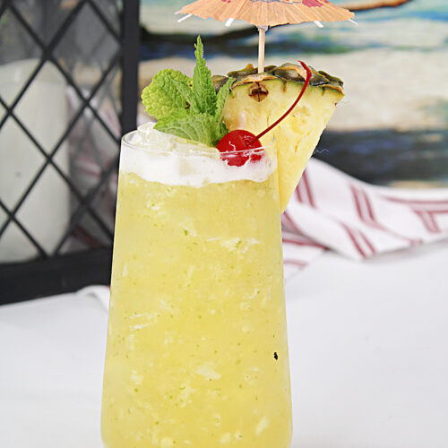 A tall glass of pineapple coconut mojito with all the flavors of the tropics! Garnished with a wedge of pineapple, maraschino cherry and an umbrella.