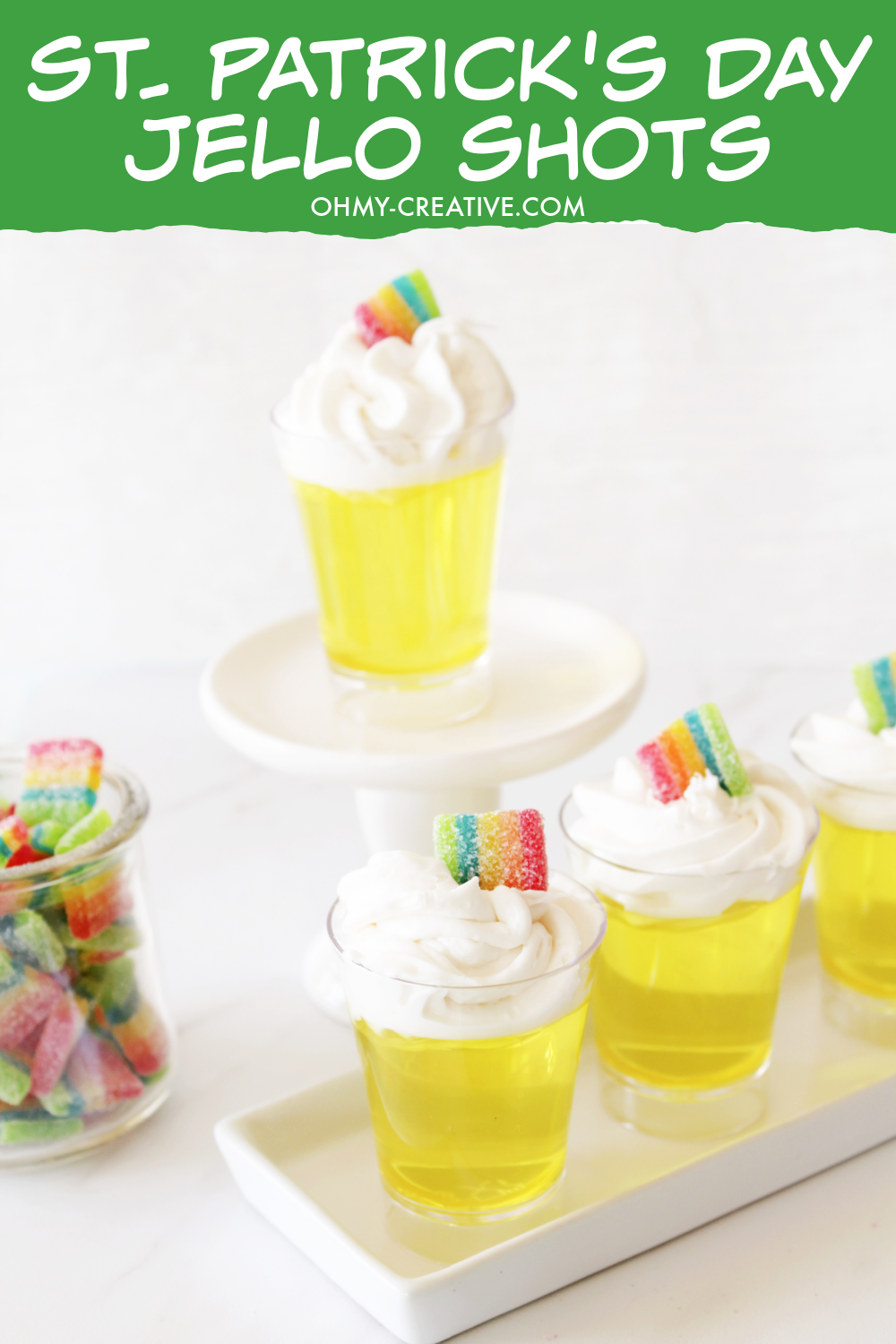 Pin image with St. Patrick's DayPot o' gold jello shots sitting on a white tray. Jar of rainbow candy sitting in the background.